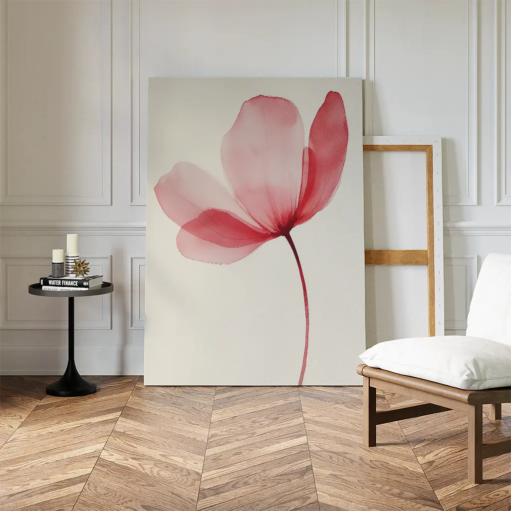 The Single Bloom Canvas Art, a minimalist floral piece with a pink flower, rests against a wall in a stylish room featuring herringbone wood floors, a white chair, and a small round table decorated with candles and books.