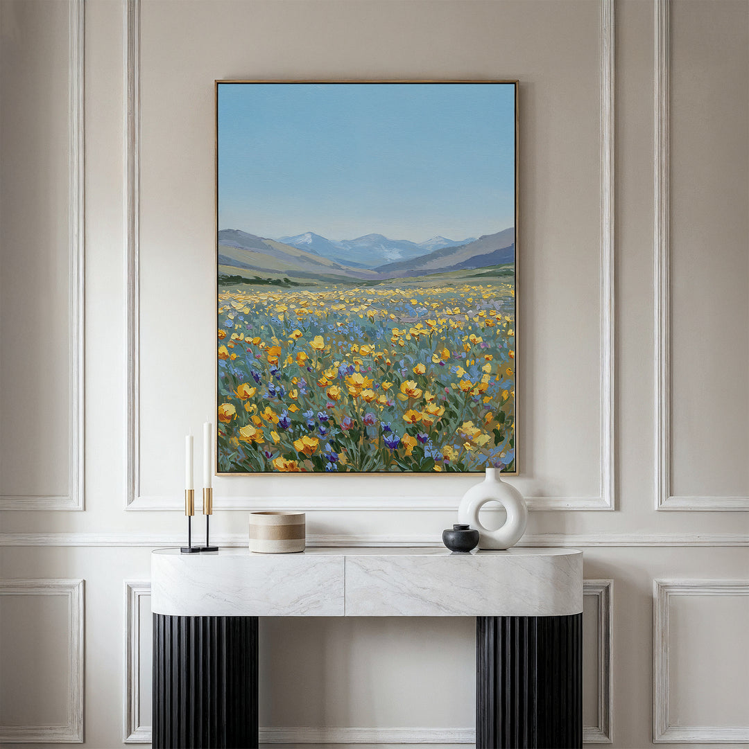 The Skyview Field Canvas Art, featuring a vibrant wildflower field with distant mountains and blue sky, hangs above a modern white and black console table in an elegant paneled room with minimalist decor.