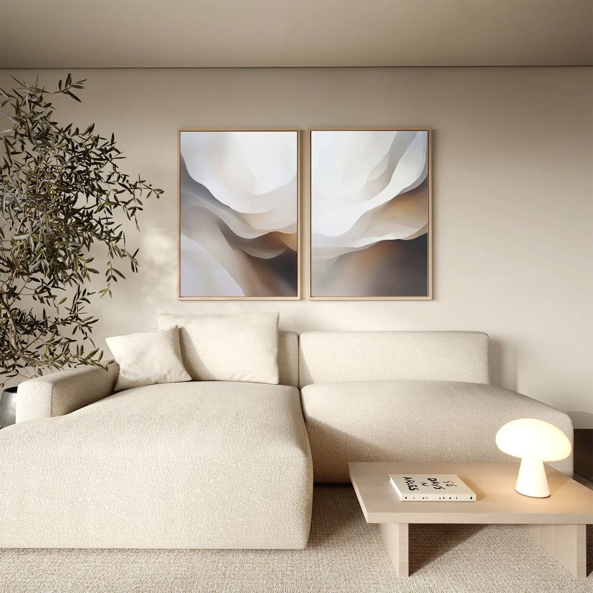 A modern living room featuring a cream sectional sofa, wooden coffee table with lamp and book, neutral decor highlighted by the Smooth Flow Set of 2 abstract wall art prints, and a leafy indoor plant in the corner.