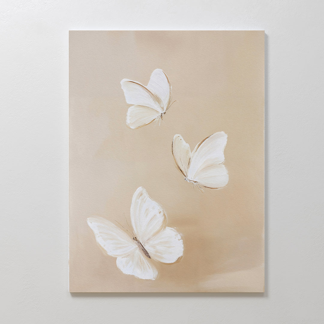 Linen Wings Canvas Art features three white butterflies with delicate wings on a light beige background. Spaced apart at various angles, this elegant piece adds gentle movement and charm to your wall decor.
