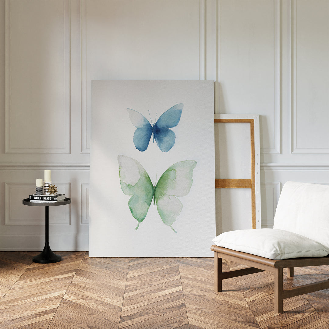 A minimalist room with herringbone floors, a cushioned chair, and a round table with candles and books. The wall features Soft Flight Canvas Art, Nordic Park-inspired minimalist art showing two watercolor butterflies in blue and green.