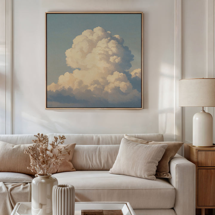A cozy, modern living room with a beige sofa, neutral pillows, a dried flower arrangement on the coffee table, a table lamp, and the Soft Skies Rising Canvas Art—a large cloudscape print—displayed above the sofa.