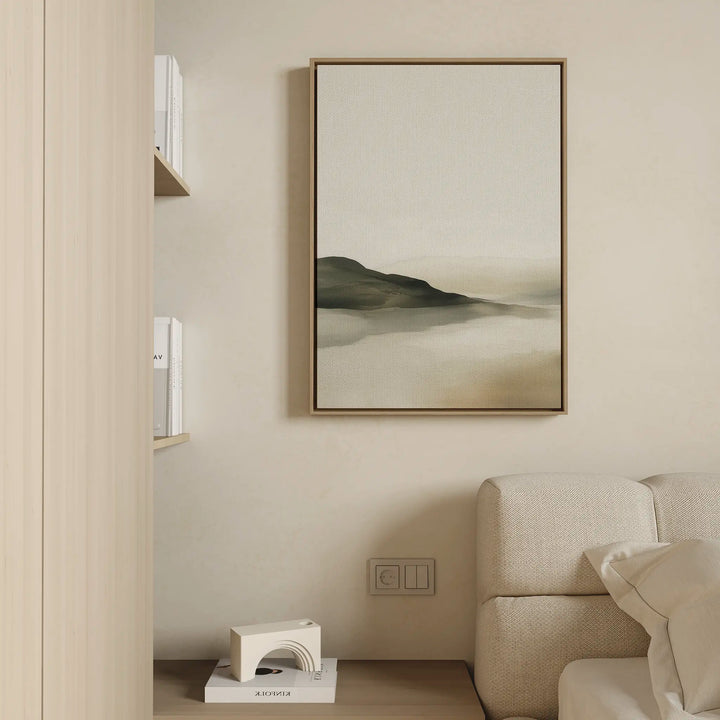 Minimalist living room with a beige sofa, light wooden bookshelf, and the Soft Valley Canvas Art – Vertical, a framed abstract painting of soft hills and misty tones, adding calming minimalist decor to the neutral wall.