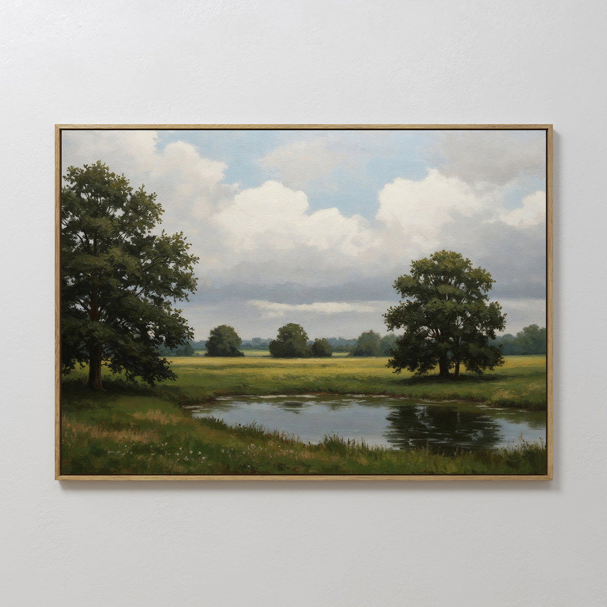 The Still Grove Canvas Art, featuring a serene grassy field, pond, leafy trees, and a cloudy sky, is displayed on a plain white wall.