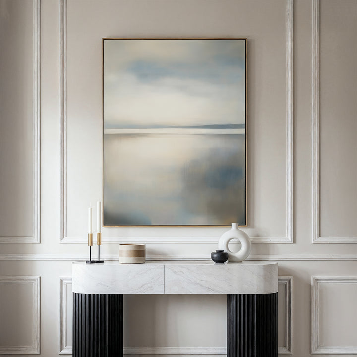 A modern interior features a white console table with minimalist decor against paneled walls. Above, the Still Horizon Canvas Art in soft neutrals adds serene, shoreline-inspired minimalism to the space.