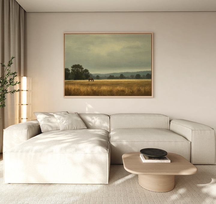 A modern living room features a beige sectional sofa, a light wood coffee table, and the Still Morning Canvas Art depicting a field with trees and a horse. Tall curtains let in natural light, enhancing the serene atmosphere.