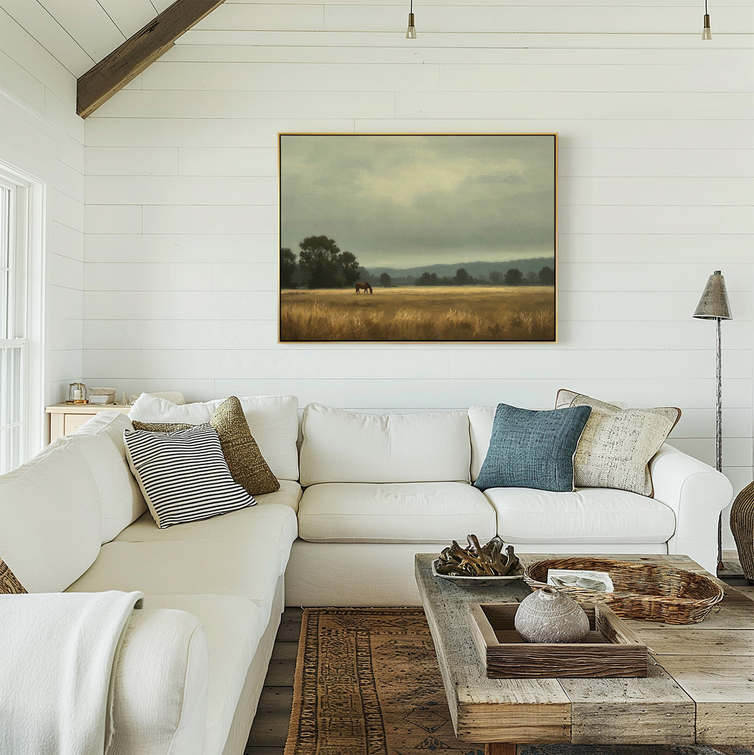 A cozy living room features a white sectional sofa with assorted throw pillows, a rustic wooden coffee table, and the Still Morning Canvas Art—a large landscape painting—hanging on a white shiplap wall.