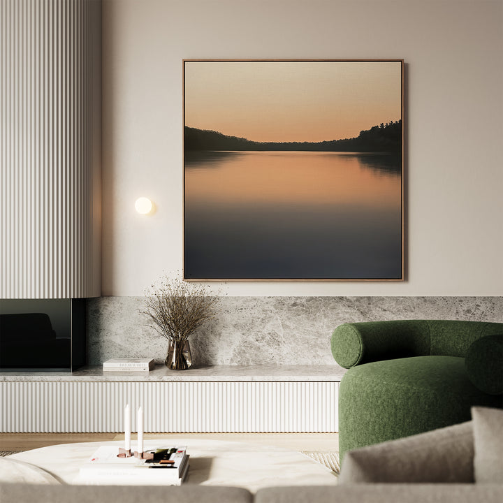 A modern living room with a green armchair, marble accents, and the Still Waters Canvas Art featuring a calm lake at sunset above a low console. A small vase with dried branches and books adds charm to the decor.