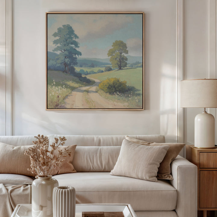A cozy living room with a white sofa, beige and cream pillows, a wooden side table with a lamp, dried flowers in a vase, and Summer Dale Canvas Art hanging above as rustic wall decor.