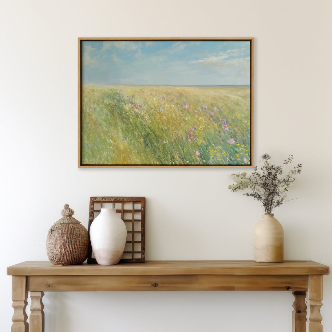 A wooden console table with decorative vases and dried flowers sits against a white wall. Above it hangs the Summers Embrace Canvas Art, featuring a sunlit wildflower field beneath a blue sky with soft clouds.