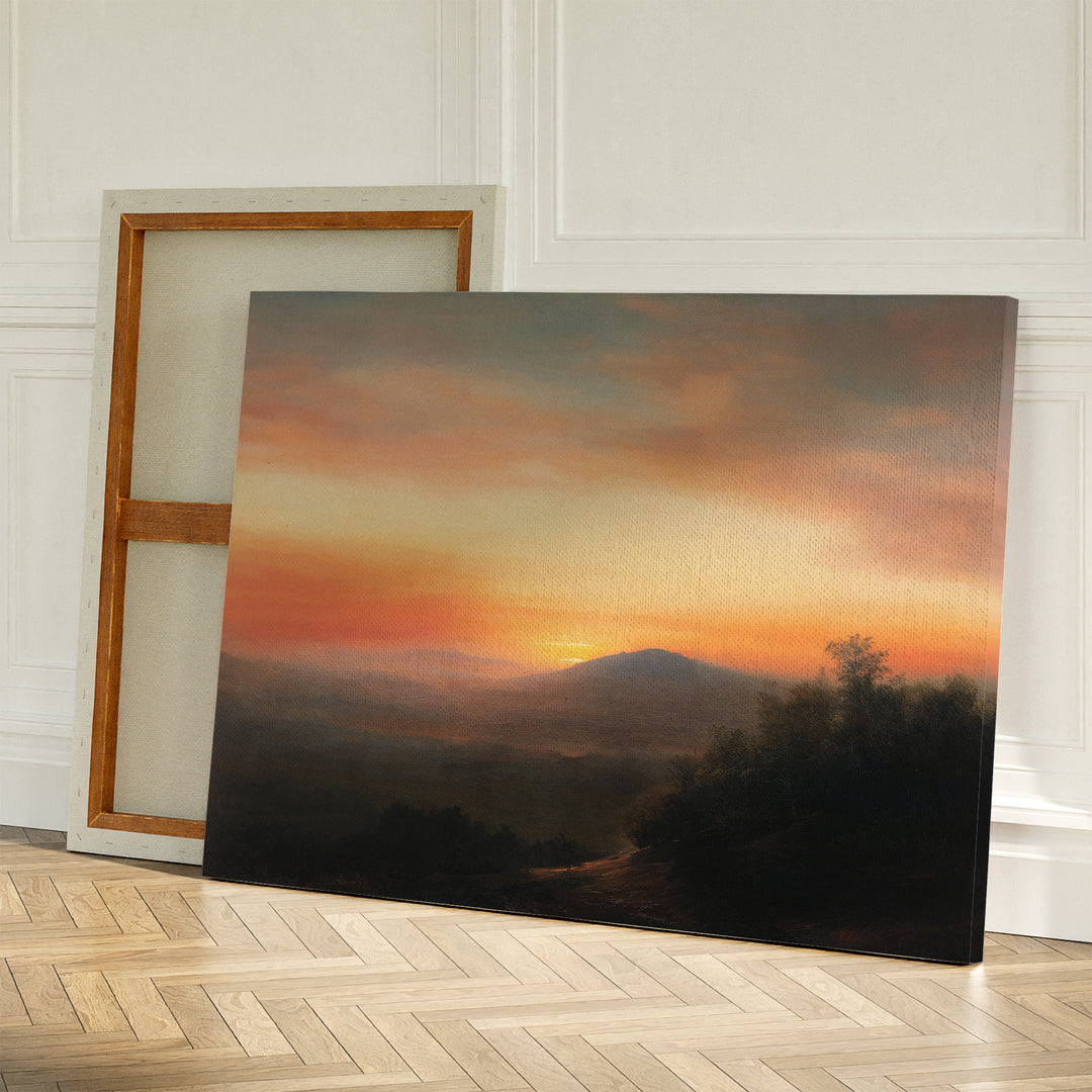 The Sunset Reflection Canvas Art, depicting a tranquil sunset over rolling hills and trees, leans against a wall on a herringbone wood floor next to a blank canvas—ideal vintage-inspired wall decor.