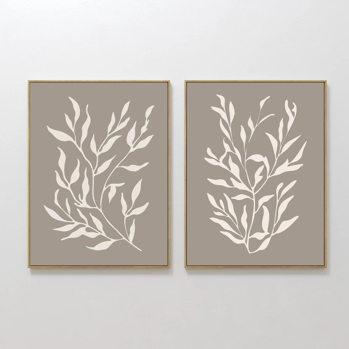 The Taupe Botanical Set of 2 features minimalist white leaf designs on beige backgrounds, displayed side by side—perfect for adding a contemporary touch to any plain white wall.