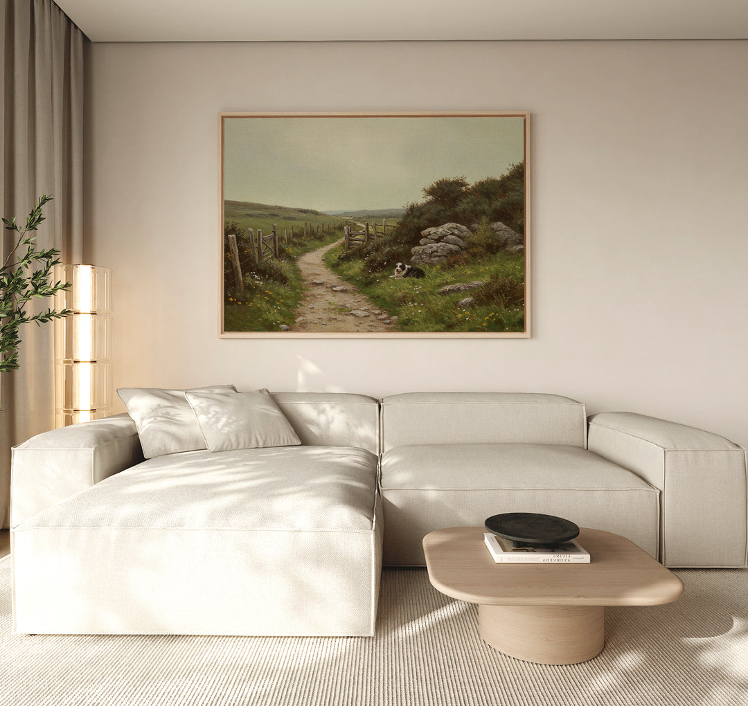 A modern living room features a light beige sectional sofa, wooden coffee table, and The Watchful Path Canvas Art depicting a rural path. Beige curtains filter sunlight, while rustic decor includes a tall plant in the corner.