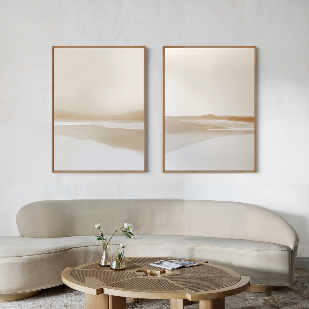 A minimalist living room features a curved beige sofa, a round wooden coffee table with vases of white flowers, and the Tranquil Horizons Set of 2 abstract landscape paintings in neutral tones on a textured white wall for an elegant touch.