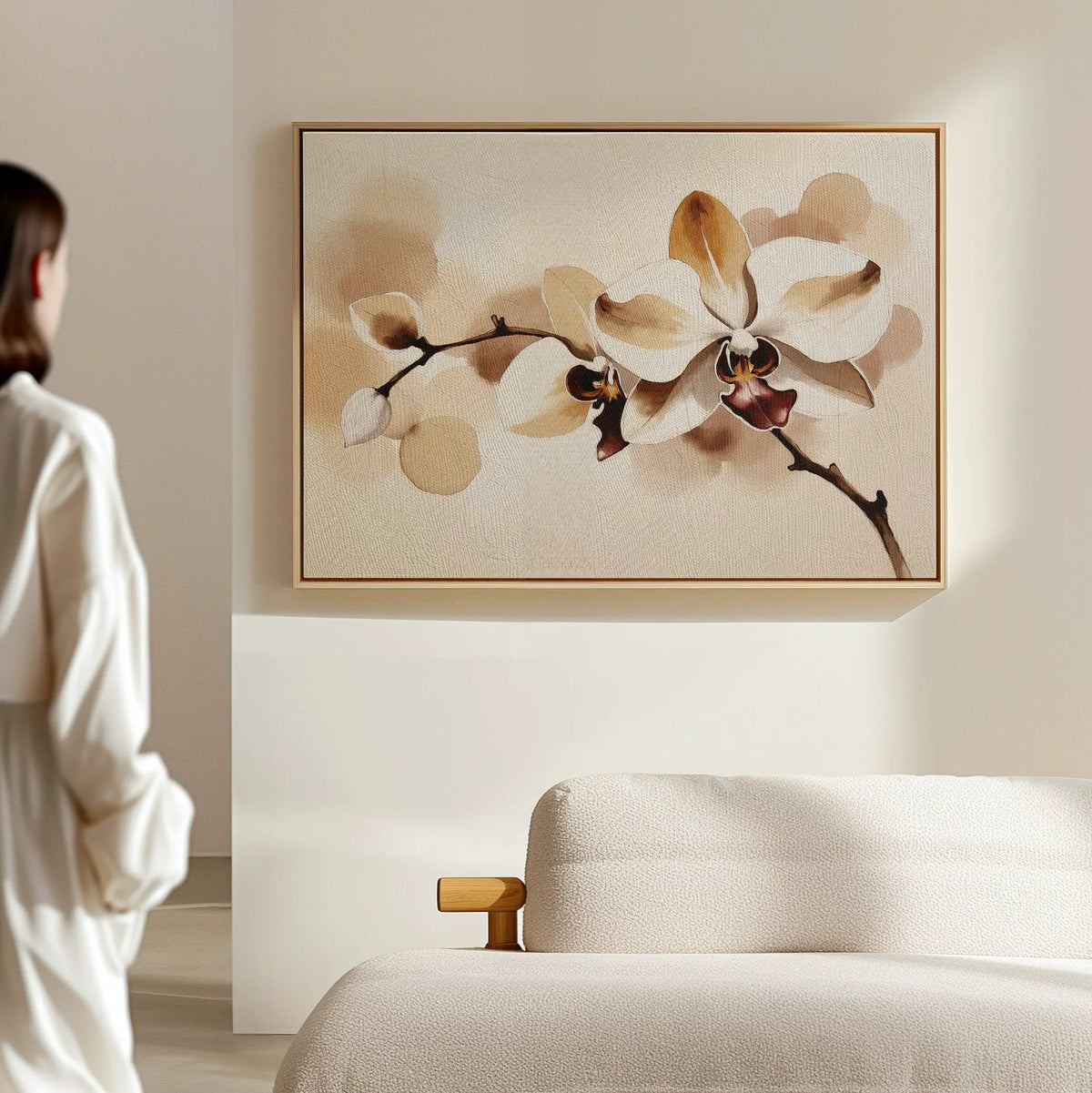 A woman in a white robe stands in a minimal, neutral-toned room, admiring the Vanilla Bloom Canvas Art—a large framed orchid print—hanging above a light-colored sofa.
