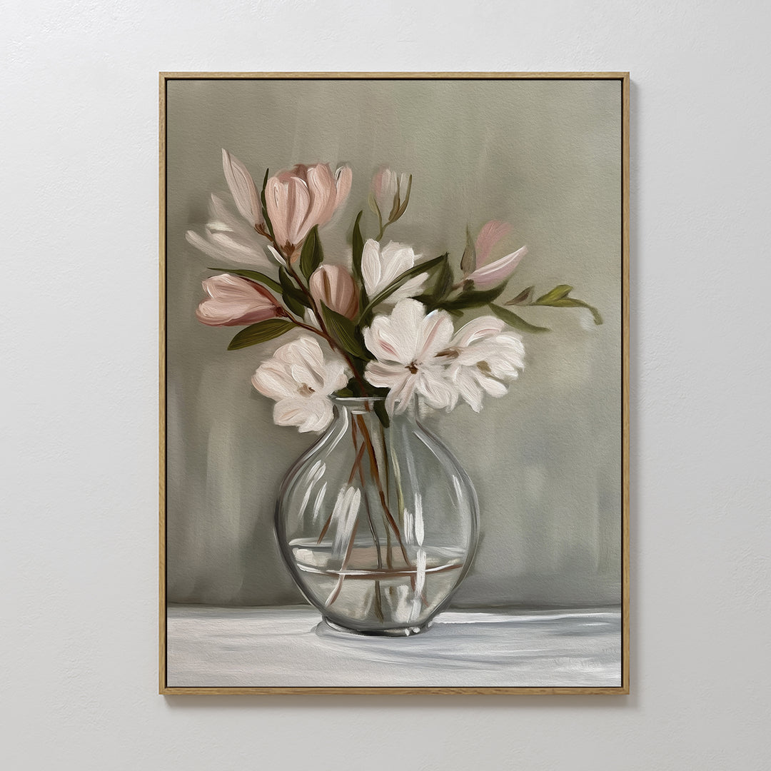 The Vase & Grace Canvas Art displays white and blush flowers in a clear vase on a white surface with a soft greenish-gray background—ideal minimalist decor for an elegant living room.