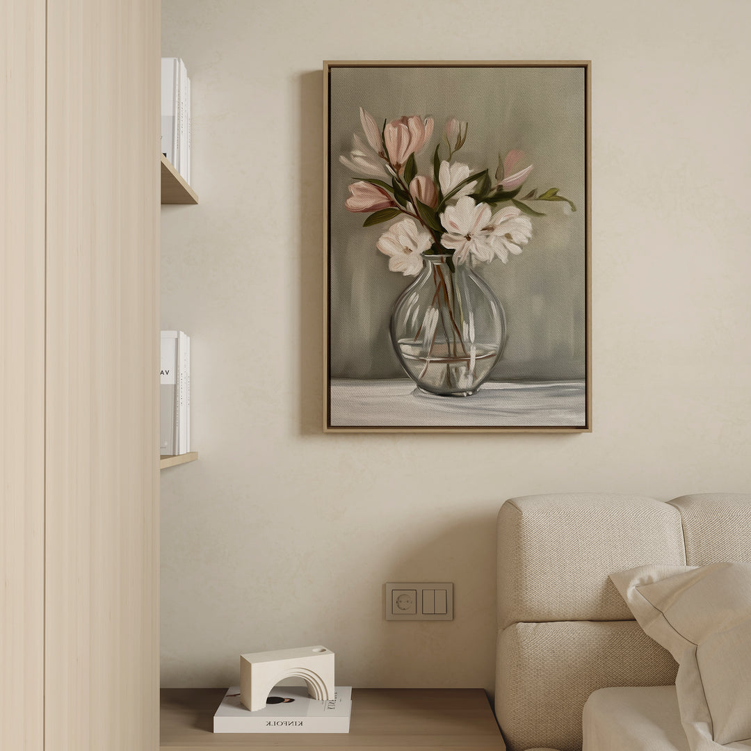 The Vase & Grace Canvas Art, featuring white and blush flowers in a clear vase, hangs above a light sofa, bringing minimalist elegance to the modern living room. Books and accents sit neatly on a nearby wooden shelf.