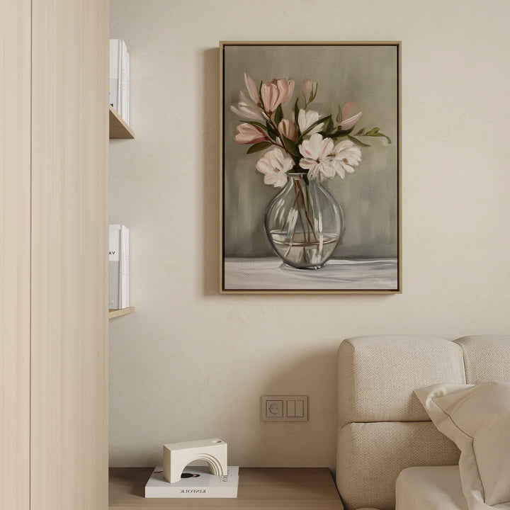 The Vase & Grace Canvas Art, featuring white and blush flowers in a clear vase, hangs above a light sofa, bringing minimalist elegance to the modern living room. Books and accents sit neatly on a nearby wooden shelf.