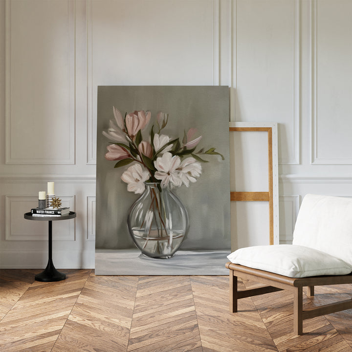 A modern, minimalist living room with chevron wood floors, white-paneled walls, a cushioned chair, a black side table with candles, and the Vase & Grace Canvas Art featuring white and blush flowers in a glass vase leaning against the wall.