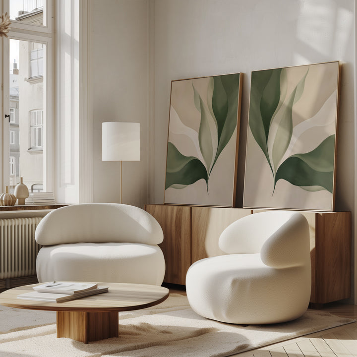 A modern living room showcases the Verdant Grace Set of 2 white rounded armchairs, a low wooden coffee table, light wood sideboard, and minimalist wall art with green leaves; sunlight brightens the space through a tall window.