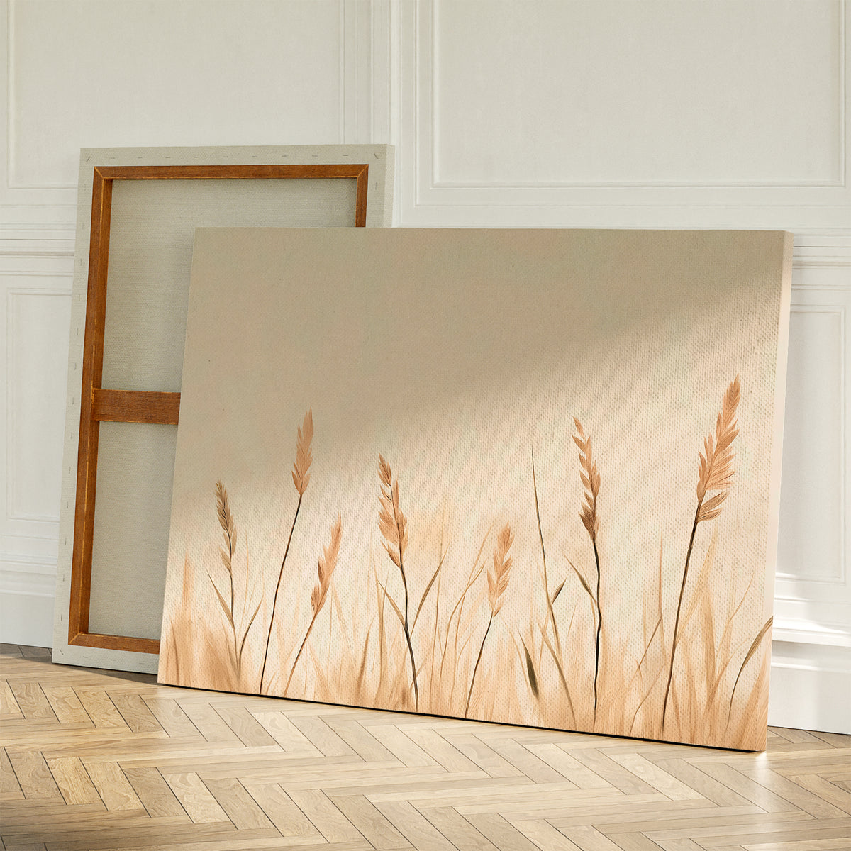 Two canvases rest on a wooden floor against a white wall; one is turned to show its frame while the other displays Whispering Reeds Canvas Art, featuring beige and brown wheat-like plants—ideal minimalist wall art for your living room decor.
