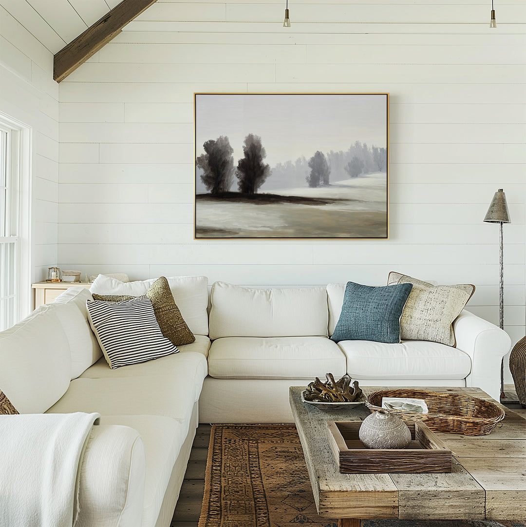 A cozy living room with a white sectional sofa, textured pillows, a rustic wooden coffee table, and neutral wall decor featuring the Winter Dusk Canvas Art of trees and foggy hills on a white shiplap wall, with natural light streaming in.