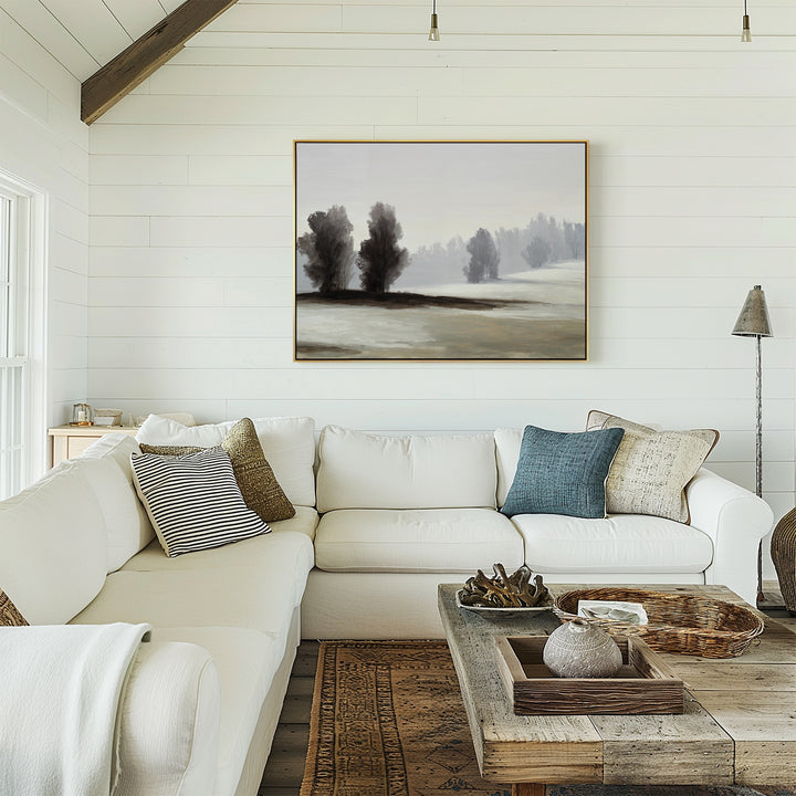 A cozy living room with a white sectional sofa, textured pillows, a rustic wooden coffee table, and neutral wall decor featuring the Winter Dusk Canvas Art of trees and foggy hills on a white shiplap wall, with natural light streaming in.