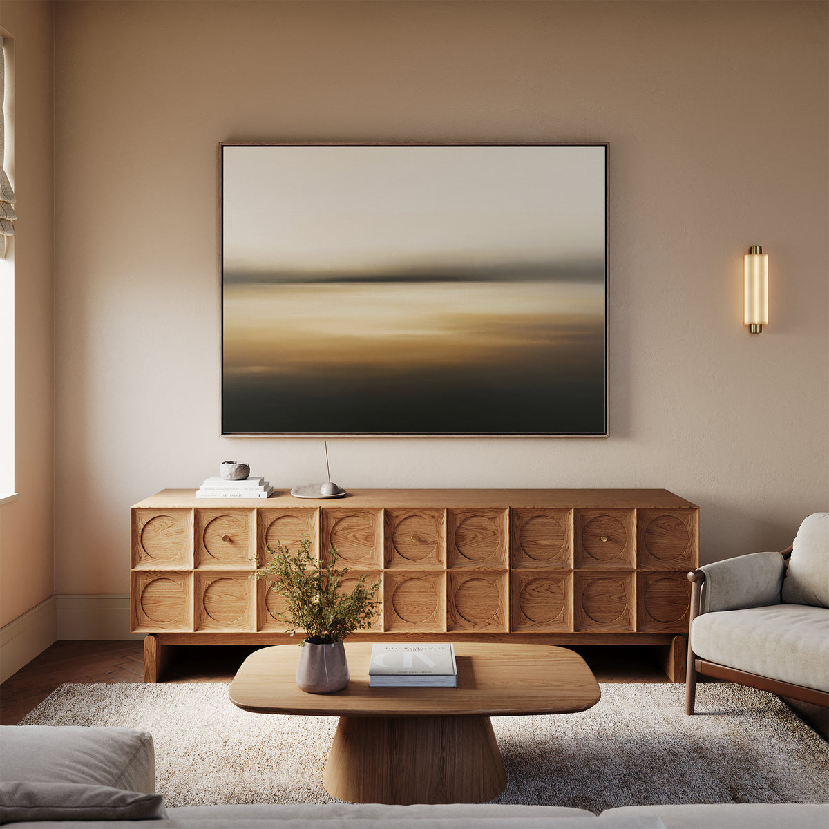 A modern living room with a beige sofa, wooden coffee table, textured sideboard, neutral-toned decor in gentle amber accents, and atmospheric “Amber Fields Canvas Art - Horizontal” wall art featuring an abstract landscape.