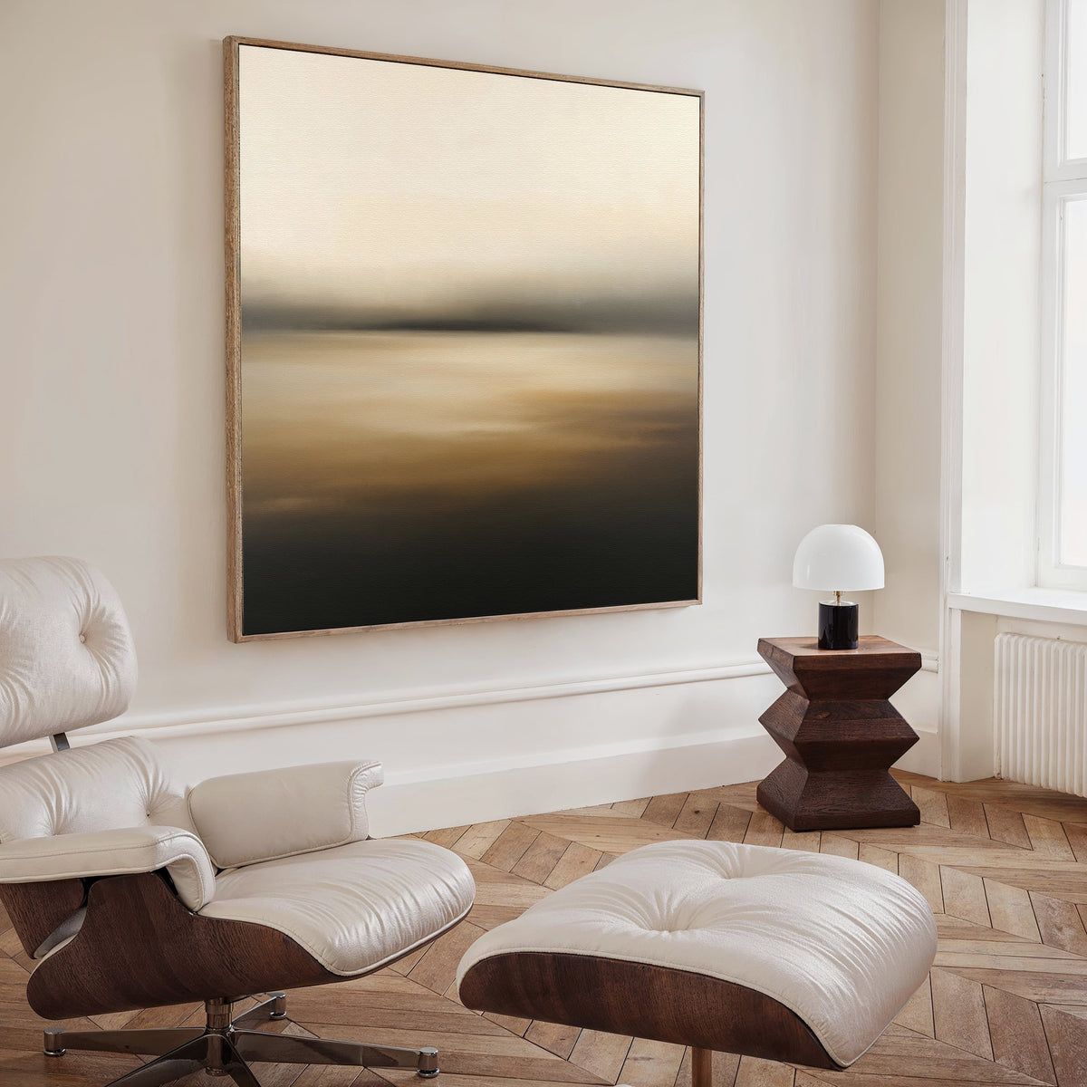 A modern, minimalist living space featuring a white leather lounge chair and ottoman, a small wooden side table with a white lamp, and the Amber Fields Canvas Art - Square in warm amber tones on the wall.