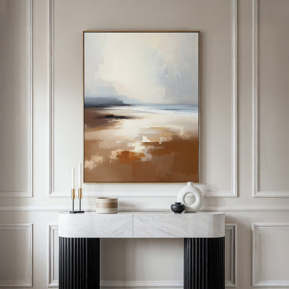 A modern console table with decorative accents stands against a paneled wall, topped by the Amber Shore Canvas Art - Vertical, featuring a tranquil abstract landscape in soft, earthy tones reminiscent of a serene beach scene.