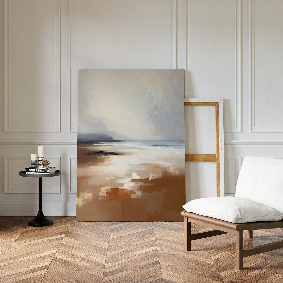 A modern, minimalist room with white paneled walls, herringbone wood floor, the Amber Shore Canvas Art - Vertical resting on the floor, an empty frame, a white cushioned chair, and a small black side table with candles and a book.