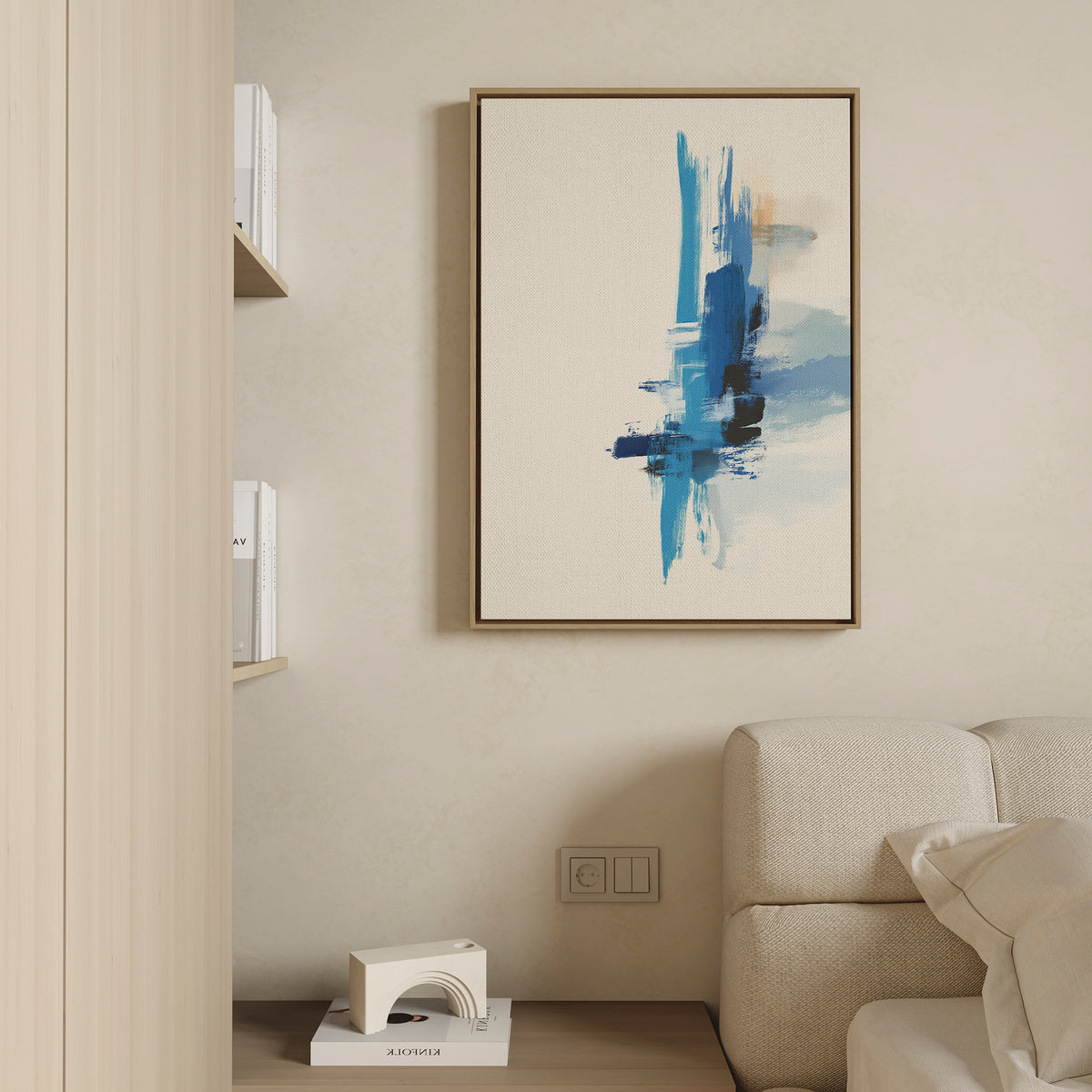 A minimalist living room features a beige sofa, a small white decor piece on a low shelf, and the Azure Convergence Canvas Art - Vertical with blue and beige brushstrokes hanging on a light-colored wall.