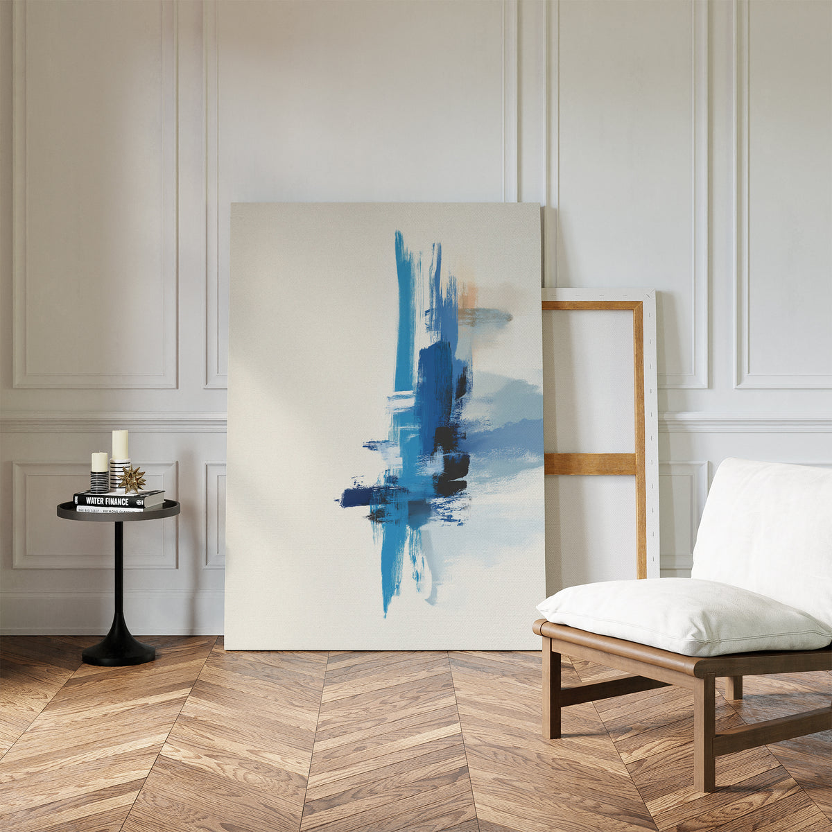 A modern living space features a white cushioned chair, a small round side table with candles and books, and the Azure Convergence Canvas Art - Vertical leaning against a white-paneled wall on herringbone wood floors.