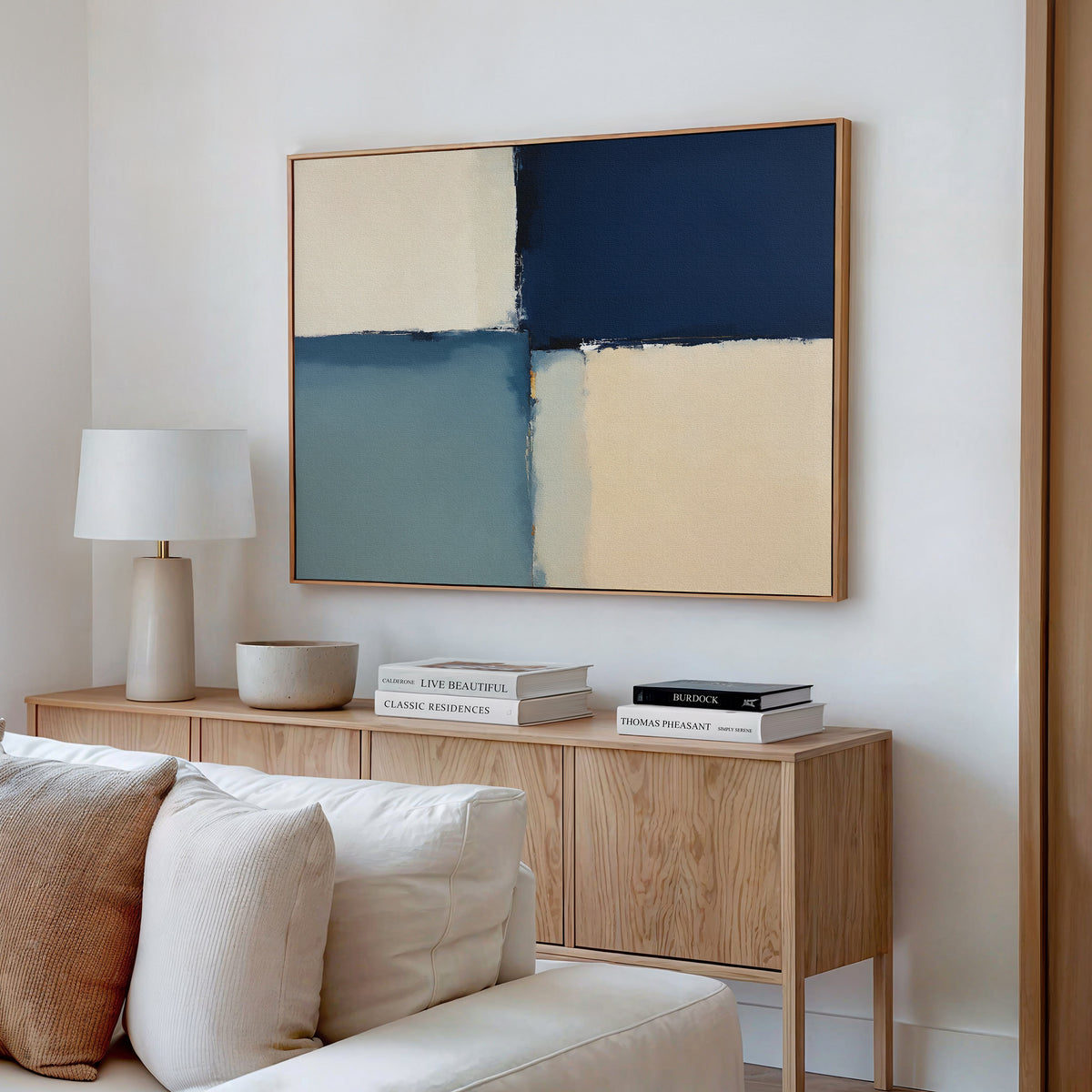 A modern living room with a wooden sideboard, books, a lamp, a bowl, and the Blue Quarters Canvas Art - Horizontal above a light-colored sofa with cushions.