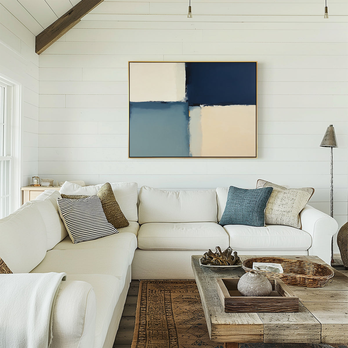 A bright living room features a white sectional sofa, textured pillows, a rustic wood coffee table, neutral décor, and the Blue Quarters Canvas Art - Horizontal with navy, blue, and cream blocks on a white shiplap wall—ideal for modern spaces.