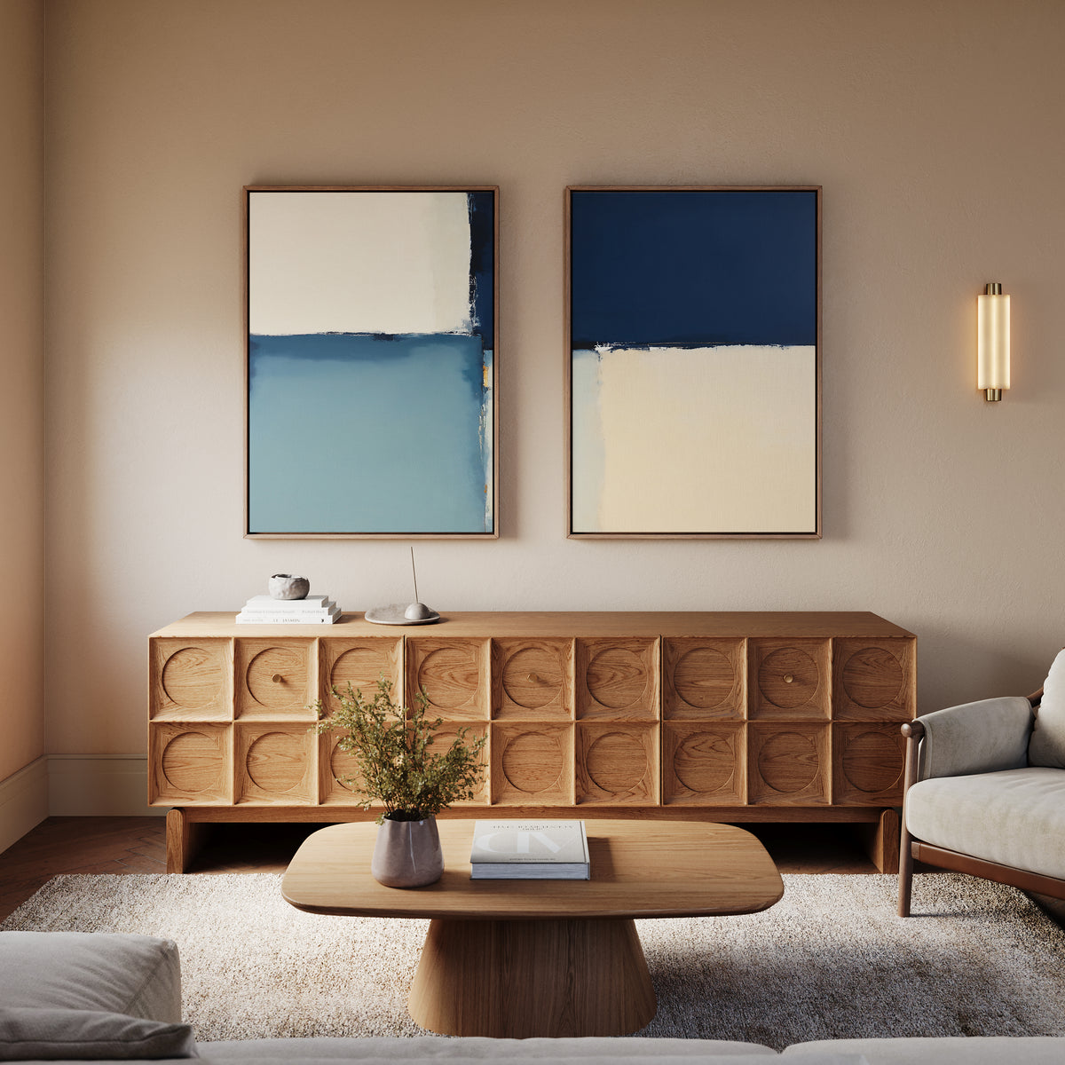 A modern living room with a light wood coffee table and sideboard, Blue Quarters - Set Of 2 abstract prints in blue and cream on the wall, a small plant on the table, and a beige sofa against a neutral wall.