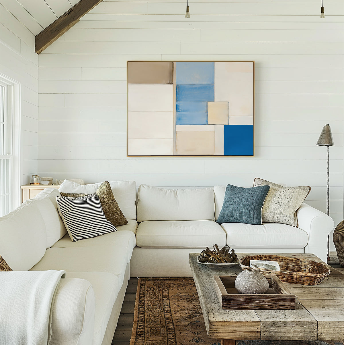 A bright living room with a white sectional, throw pillows, a rustic coffee table, and the Blue Tiles Composition Canvas Art - Horizontal featuring neutral and blue blocks—perfect for modern living room decor.