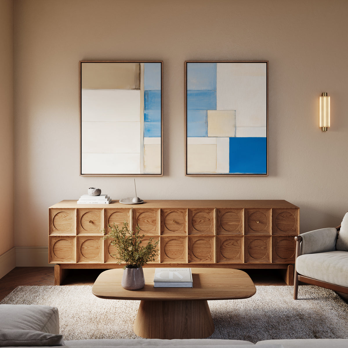 A modern living room features a wooden sideboard, "Blue Tiles Composition - Set Of 2" wall art above, a light wood coffee table with books and a vase, an armchair, and soft lighting in neutral and blue tones for a fresh, inviting feel.