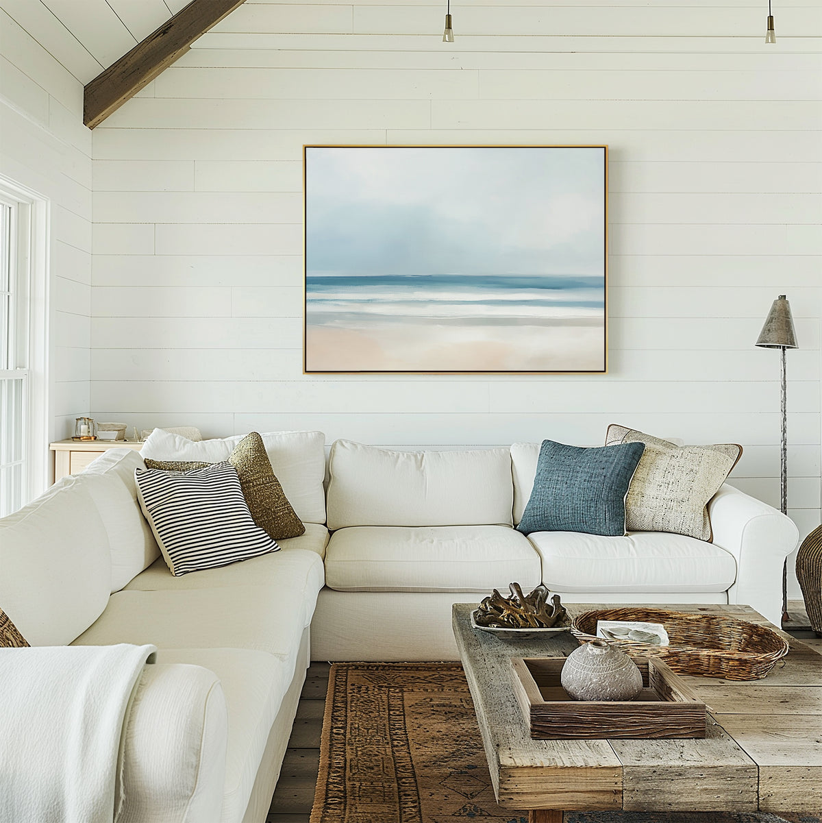 A bright, airy living room with white shiplap walls features a white sectional sofa with assorted throw pillows, a rustic wooden coffee table, and the Blurred Beach Scene Canvas Art - Horizontal above the couch.