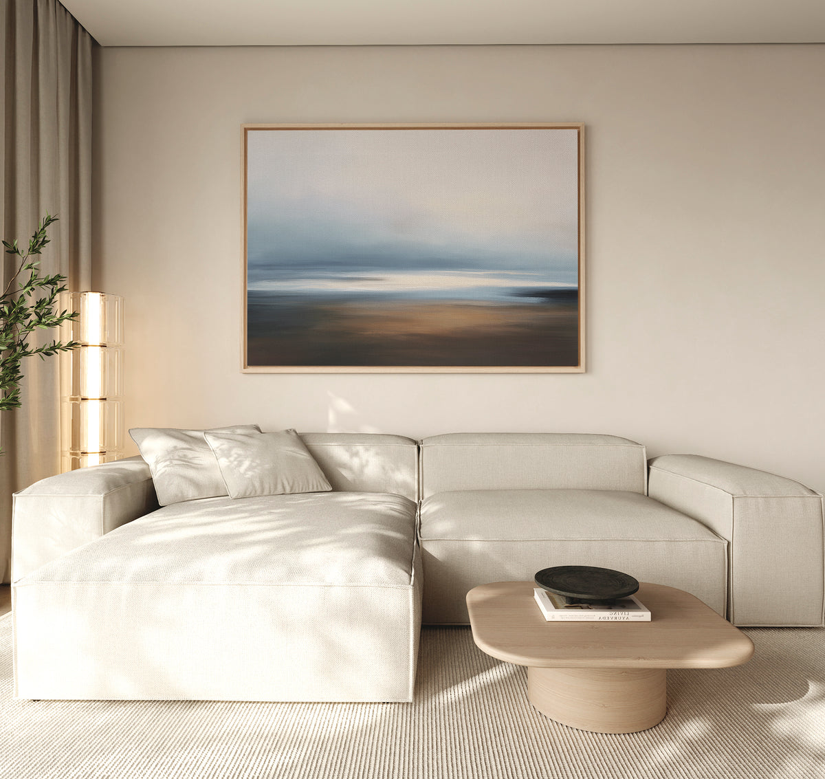 A modern living room with a light beige sectional, round wooden coffee table with a black bowl, tall plant, and the Blurred Seascape Canvas Art - Horizontal above the sofa for a touch of coastal serenity.