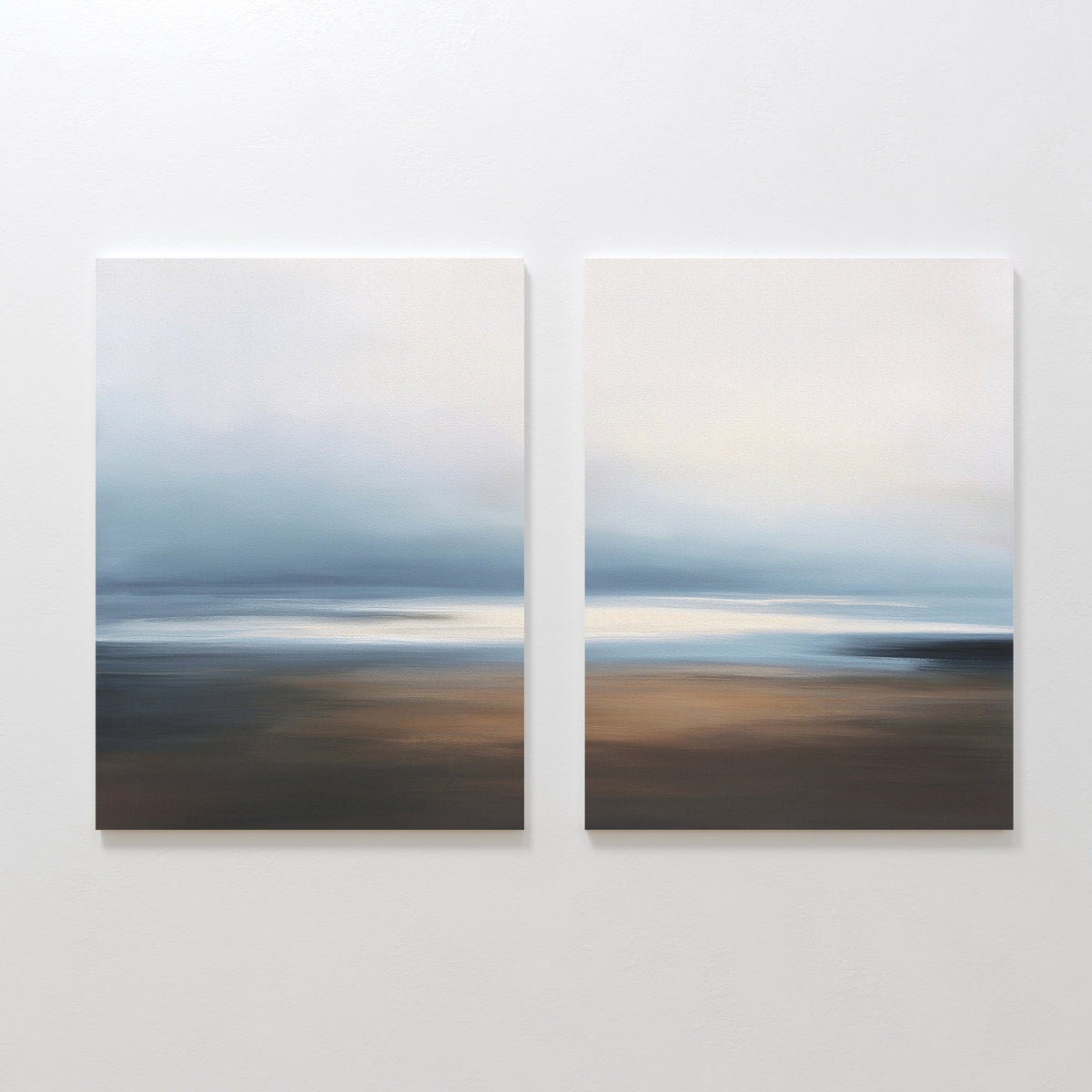 The "Blurred Seascape - Set Of 2" features abstract art prints with soft, blurred horizontal bands of blue, white, and brown, capturing a dreamy coastal vibe and adding serene decor to any wall.