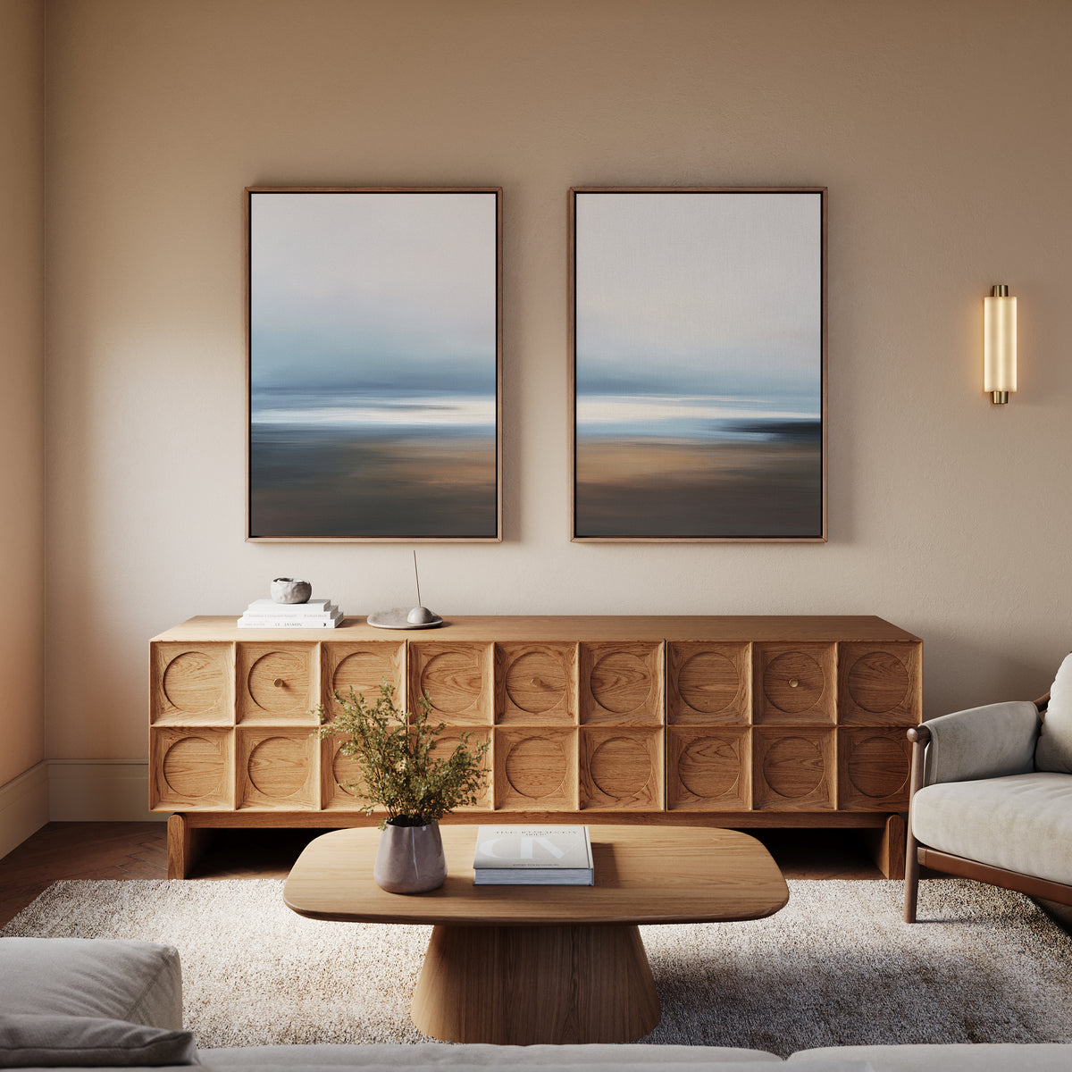 A modern living room with light walls, a wooden sideboard with geometric patterns, a wooden coffee table, a light sofa, a plant, and the "Blurred Seascape - Set Of 2" wall art above the sideboard for coastal serenity.