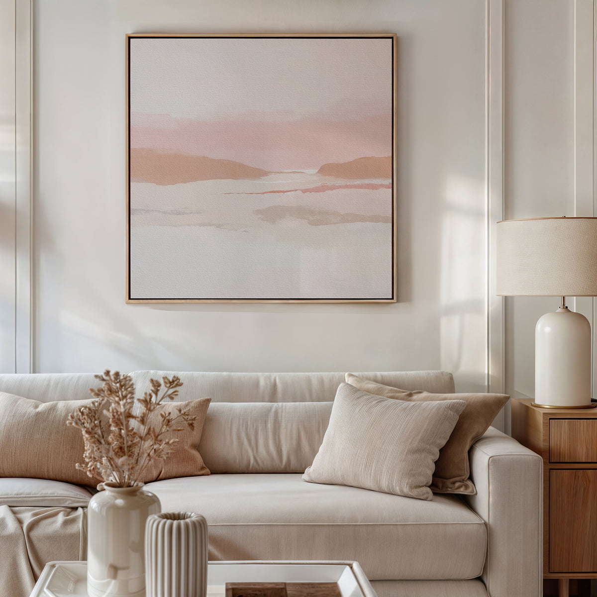 A modern living room with a beige sofa, neutral pillows, light wood side table, lamp, dried flowers in a vase, and the Blush Mesa Canvas Art - Square on the wall. Warm natural light fills the softly-toned space.