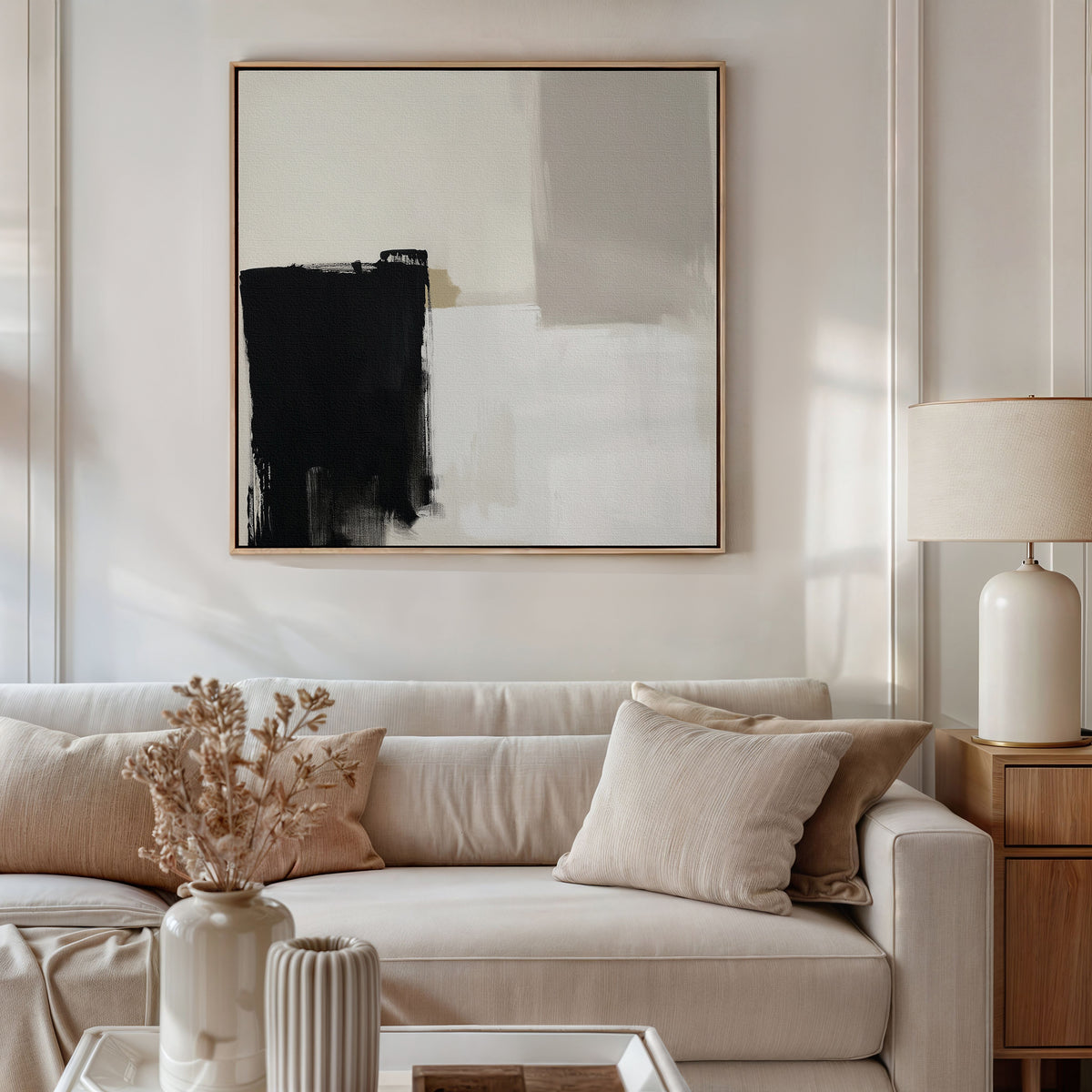 A modern living room featuring a beige sofa, neutral pillows, a wooden side table with a ceramic lamp, dried flowers in a vase, and the Bold Division Canvas Art - Square on the wall elevates contemporary style.