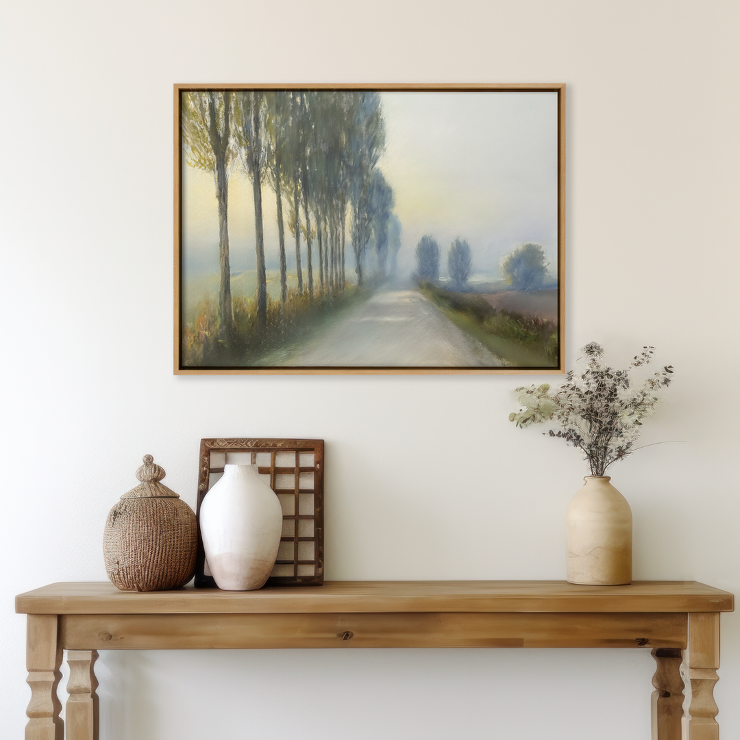 A wooden console table with vases and decor stands against a white wall, beneath the Forest Haze Canvas Art—a framed painting featuring a serene, tree-lined country road in soft, muted tones.