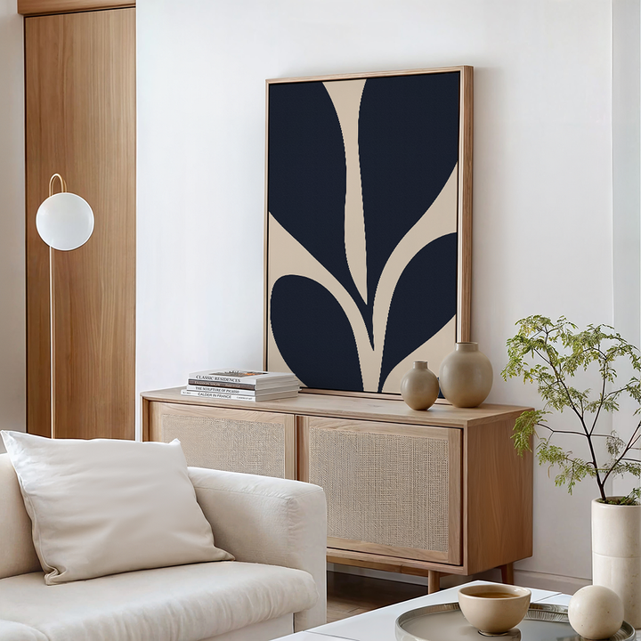 A modern living room with neutral tones features a light wood sideboard, Botanical Ink Abstract Canvas Art in beige and navy, ceramic vases, books, a white sofa with cushions, a round coffee table, and a leafy plant—perfect for stylish decor.