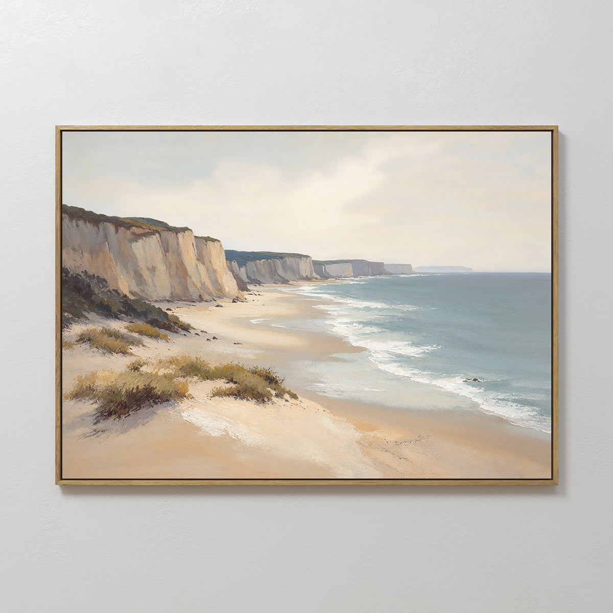 Chalk Shores Canvas Art - Horizontal: A framed canvas print depicting sandy cliffs, gentle waves, and sparse greenery beneath a cloudy sky—ideal seaside decor for a plain white wall.