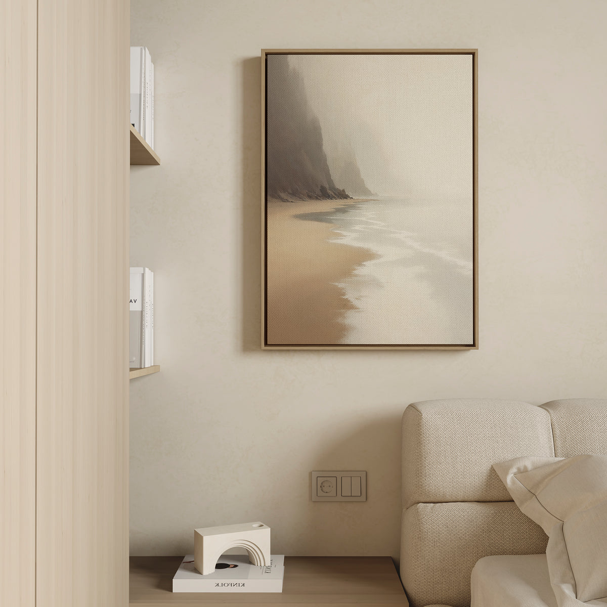 The Coastal Silence Canvas Art - Vertical hangs framed on a beige wall above a light sofa, while nearby shelves with books and decor add to the minimalist, neutral aesthetic inspired by coastal wall art.