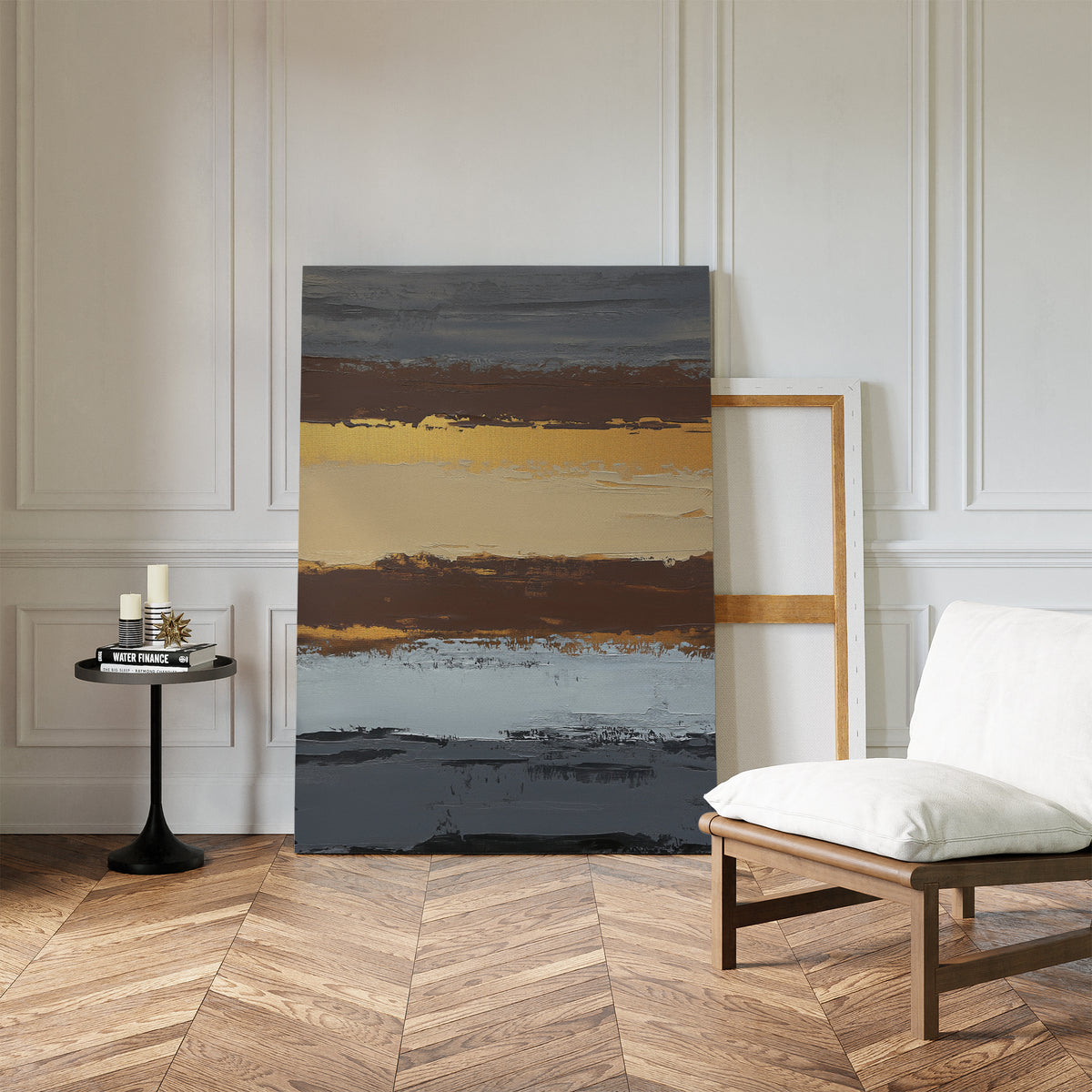 A modern room with earthy elegance showcases the Coastal Strata Canvas Art - Vertical beside a white cushioned chair, a round black table with candles and books, all set against a white paneled wall on wood flooring.