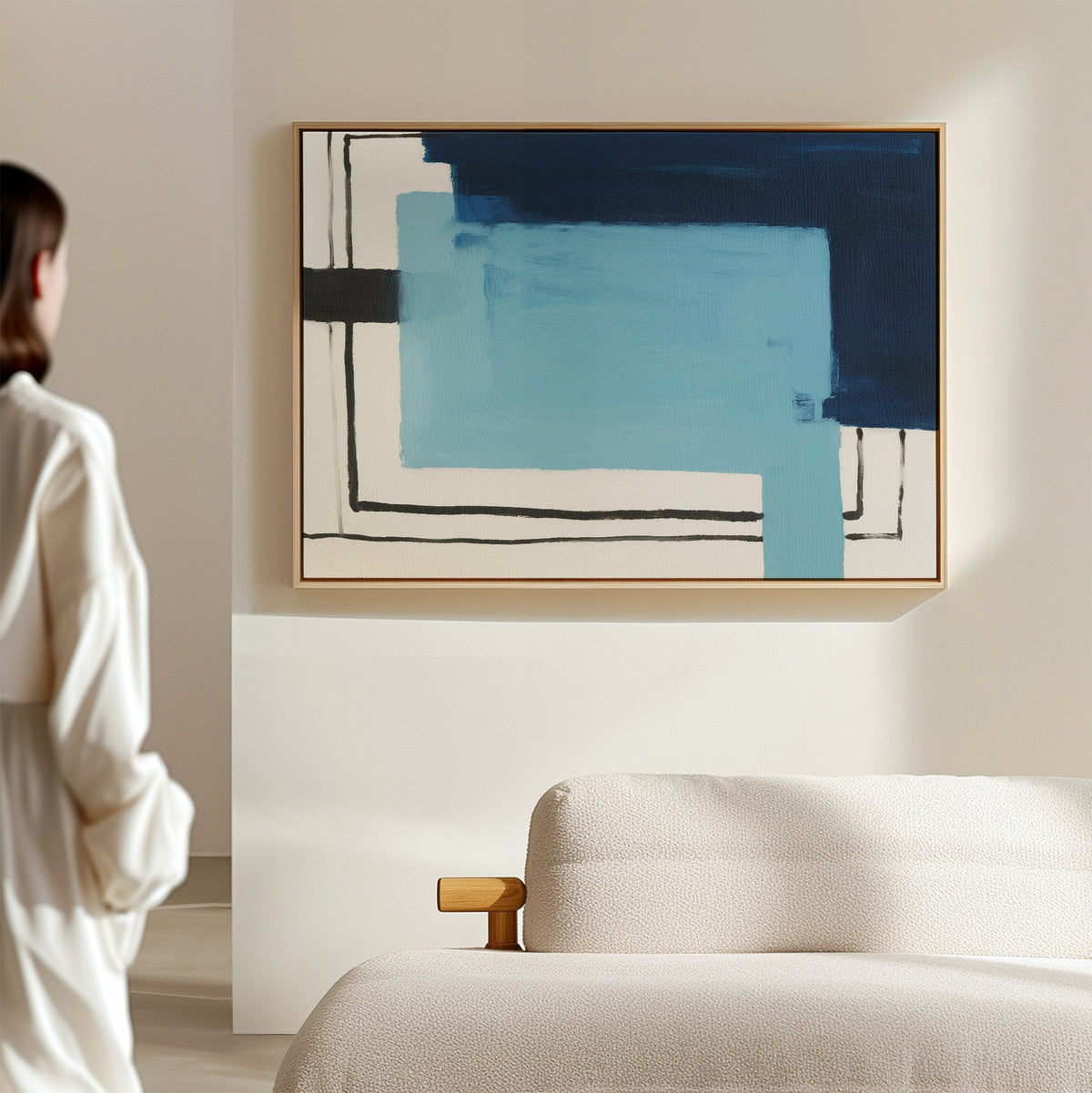 A person stands in a minimalistic room, admiring the Cobalt Intersection Canvas Art - Horizontal featuring blue and black shapes, displayed above a beige sofa on a light-colored wall.